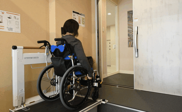 2.車いす利用者がリモコン操作で段差解消機を使用し、玄関まで昇っている様子